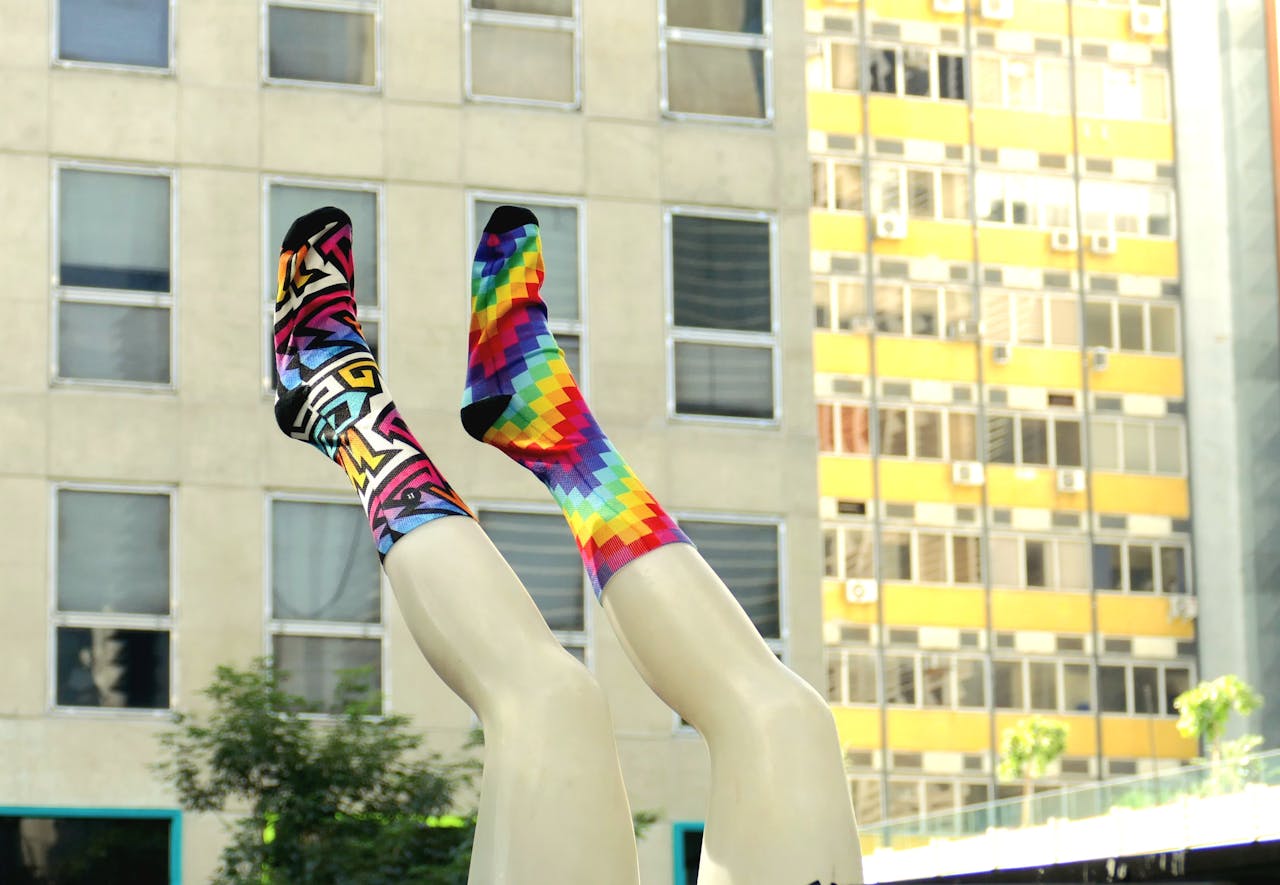 Vibrant patterned socks on mannequin legs set against urban building backdrop in São Paulo, Brazil.
