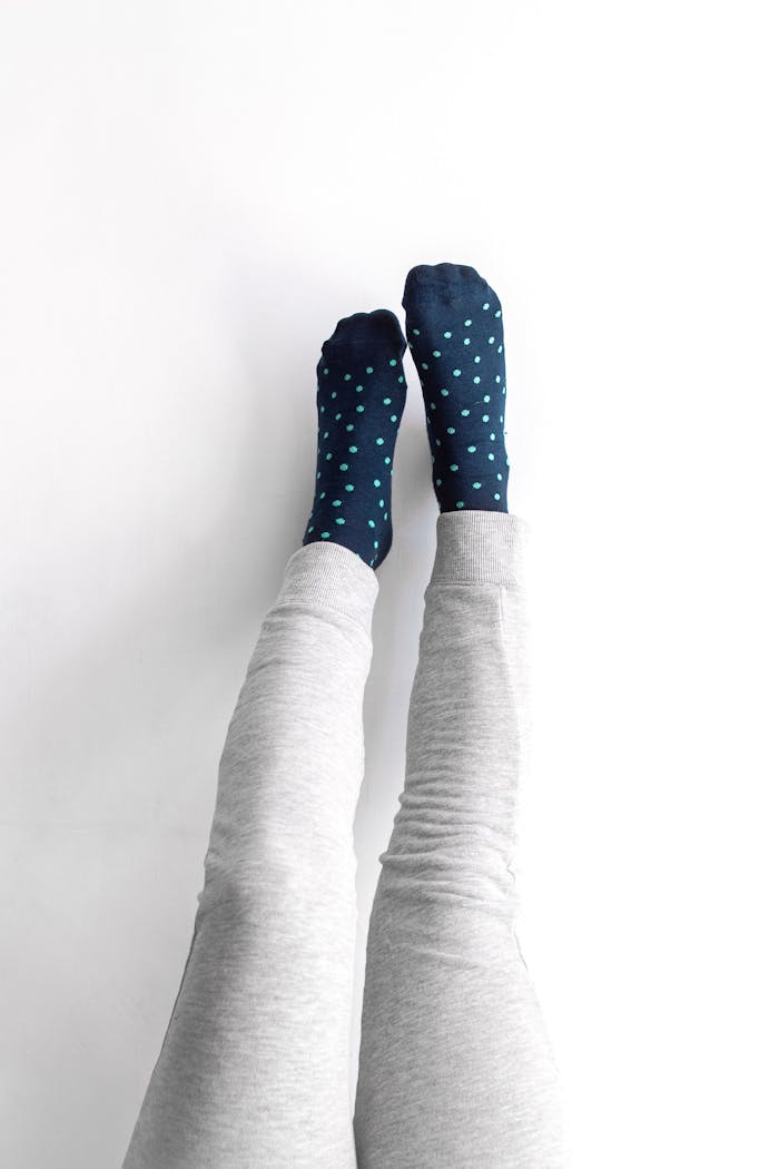 Legs in playful pose with blue polka dot socks and gray pants on white background.
