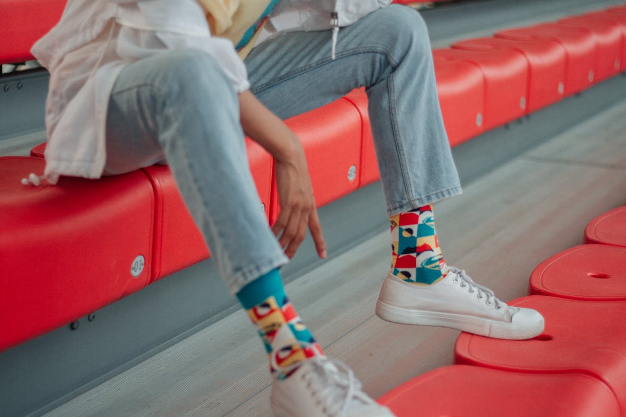 A stylish individual sits on red bleachers, showcasing colorful socks and white sneakers.