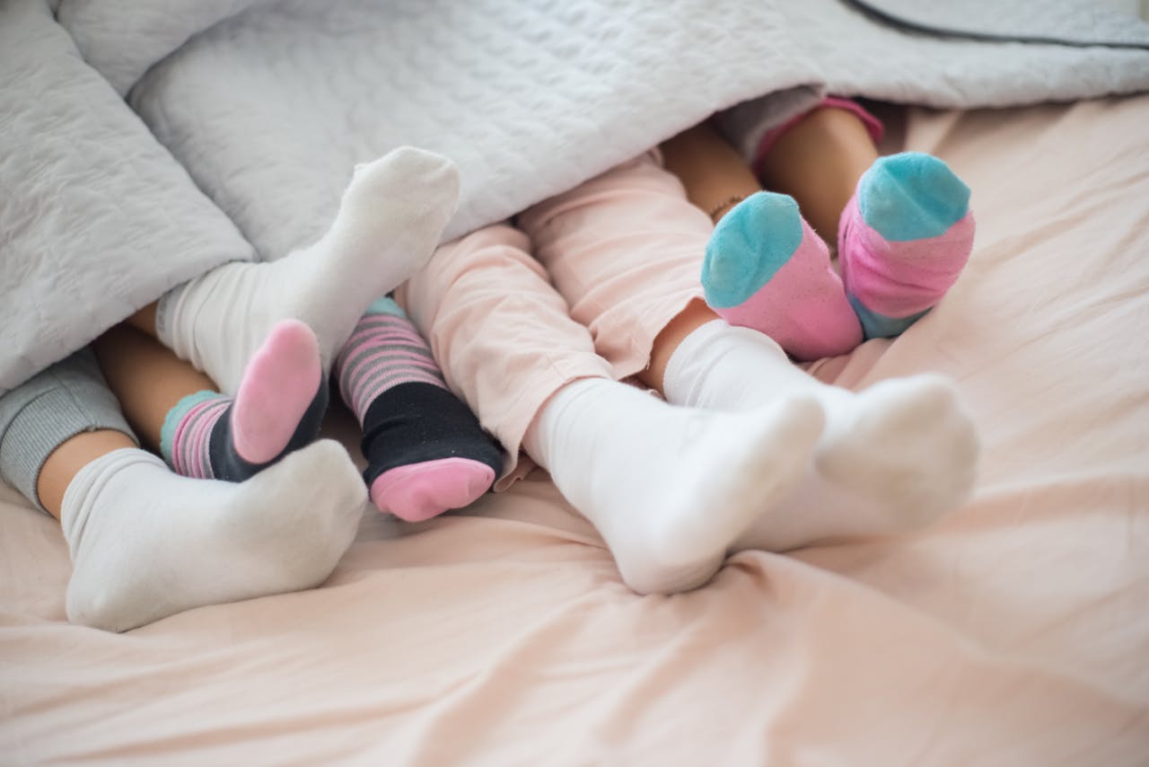 Three children under a warm duvet with colorful socks showing, creating a cozy scene.