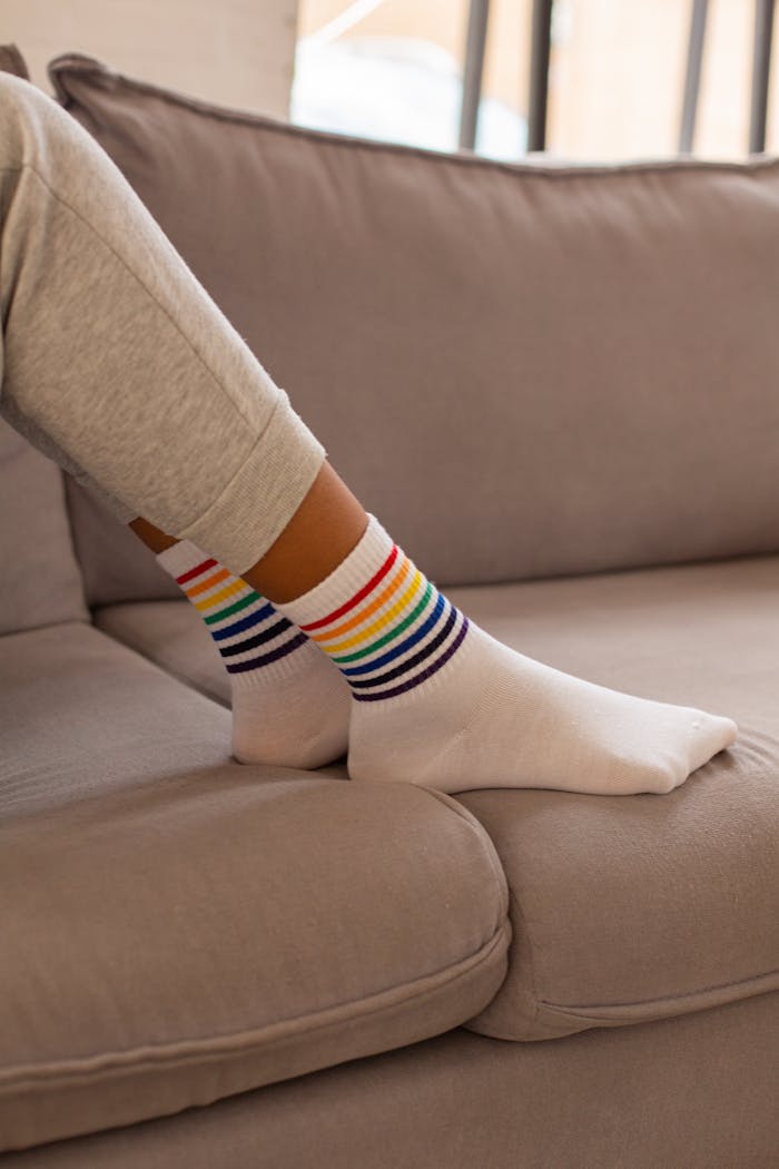 Close-up of a person wearing rainbow-striped socks on a sofa indoors.